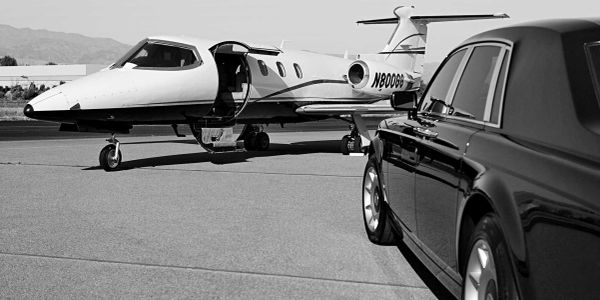 Private jet and luxury car parked on a runway under clear skies.
