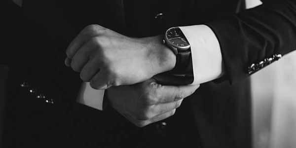 Man adjusting his wristwatch while wearing a suit in black and white.