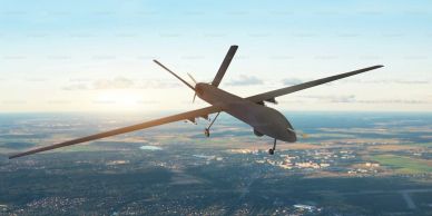 Military drone flying over landscape at sunset.