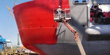 Worker painting a ship's hull red.