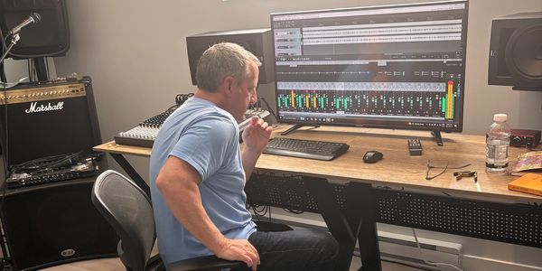 Man concentrating on audio mixing with headphones and computer.