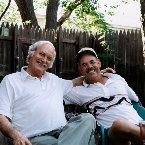 Two older men smiling and sitting together outdoors.