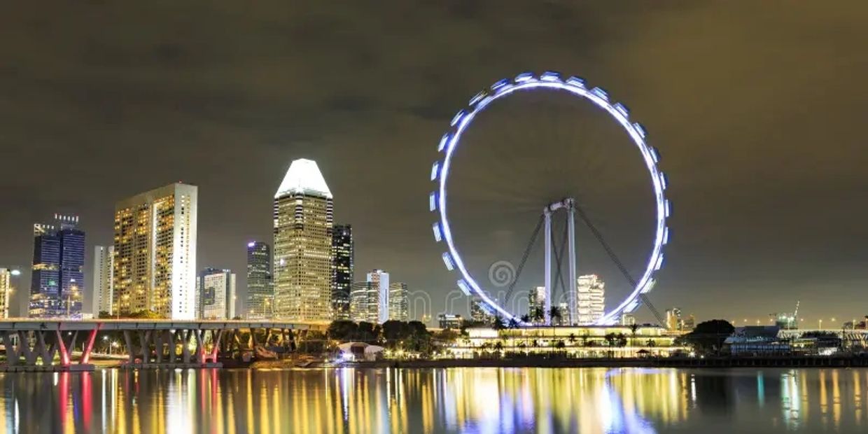 Night cityscape with illuminated Ferris wheel reflecting on water.