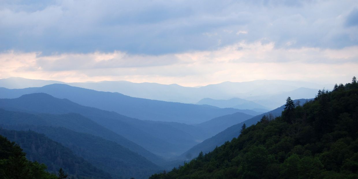 Layered mountain ranges under a cloudy sky at dusk.