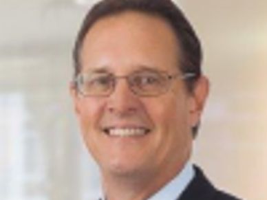 Man wearing glasses and suit smiling.