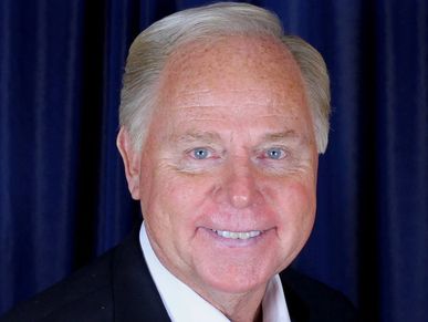 Smiling elderly man with light hair in formal attire.
