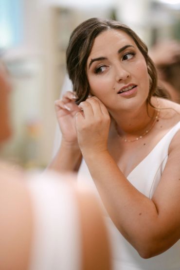 Woman adjusting earring in mirror.