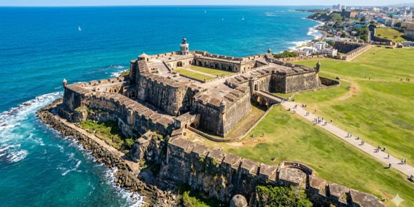Aerial view of a historic coastal fortress surrounded by ocean and green fields.