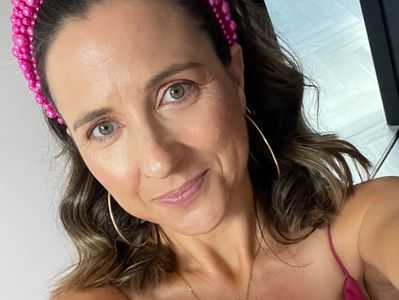 Woman smiling with a pink headband and hoop earrings.