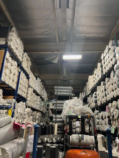 Onsite warehouse. Large building. Rolls of denim line the walls. Forklift in foreground