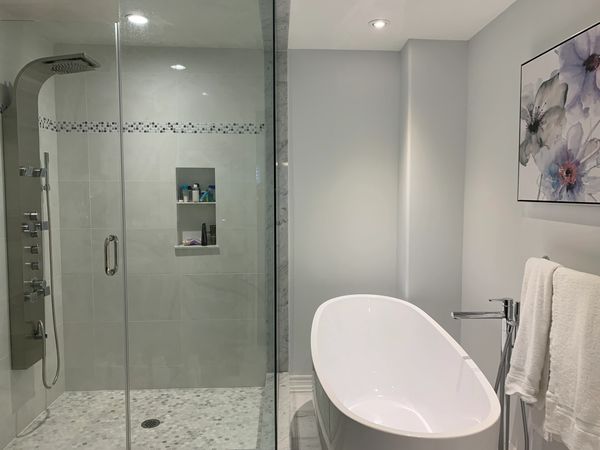 Elegant modern bathroom renovation with a glass walk-in shower, pebble floor, and freestanding tub.