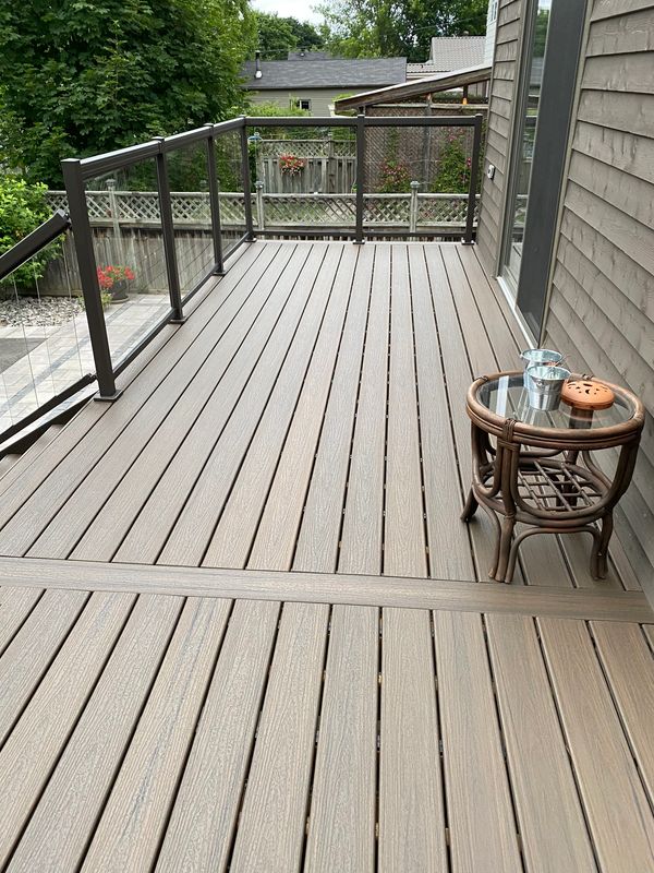 Beautiful modern composite deck renovation featuring sleek glass railings and a small patio table.