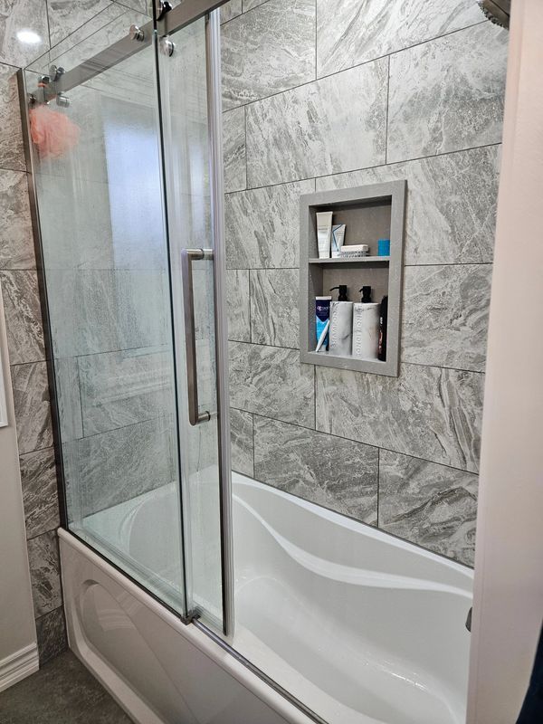 Modern bathroom remodel featuring a bathtub with glass sliding doors and grey marble-look tile.