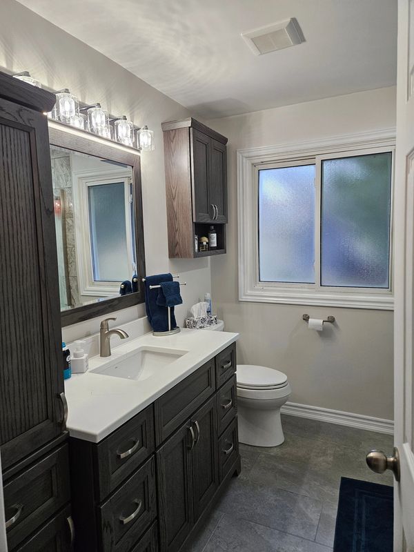 Modern bathroom remodel with a dark wood vanity, white countertop, and frosted glass window.