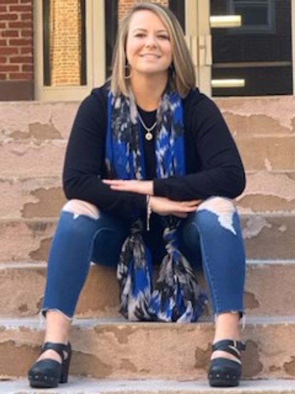 Woman sitting on stone steps wearing ripped jeans and a blue scarf.