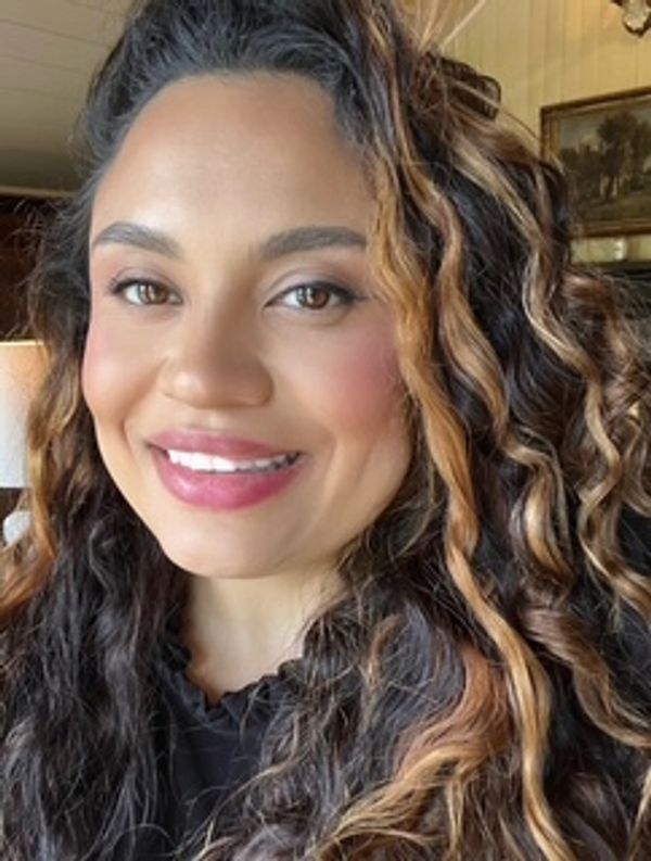 Close-up portrait of a smiling woman with curly hair and warm makeup.