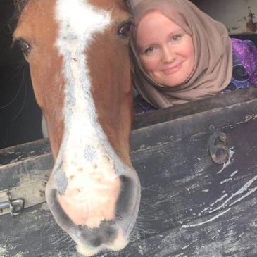 A woman smiling whilst next to a friendly horse.