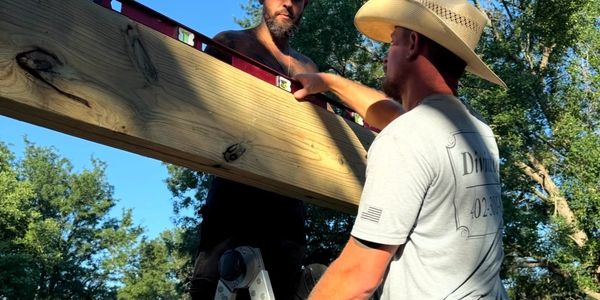 Two men working with wooden beams outdoors.