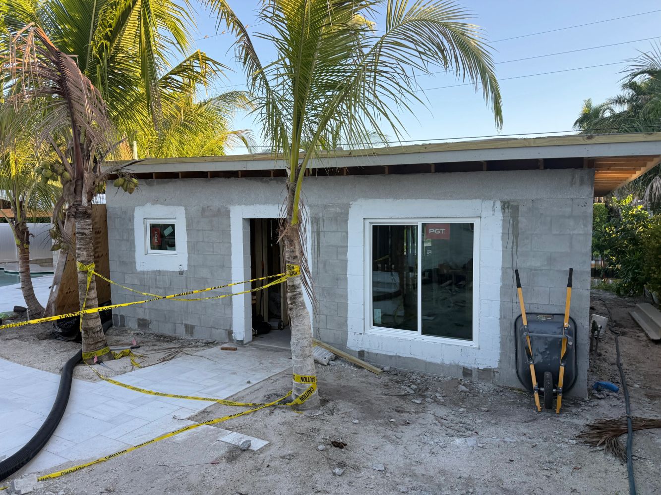 Construction site of a small building with palm trees and caution tape.