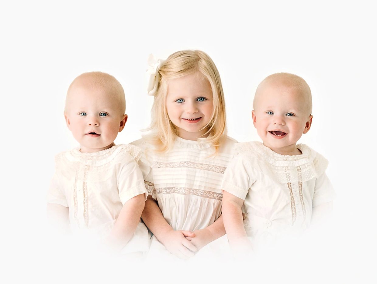 Three young children dressed in white, smiling.