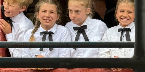 Four children in white shirts with black bow ties smiling and looking around.
