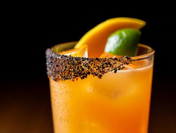 Orange cocktail with a spiced rim and fruit garnish.