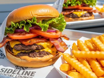 Two bacon cheeseburgers with lettuce, tomato, and onions served with crinkle-cut fries.