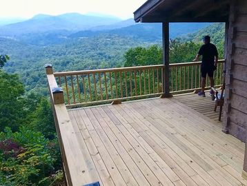 Man standing on a wooden deck overlooking mountains.