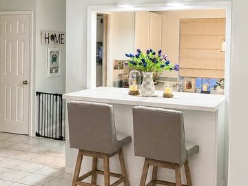 Modern kitchen breakfast bar with beige chairs and purple flowers.