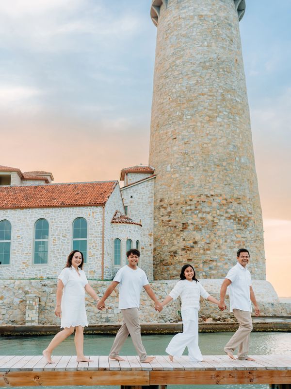 A family holding hands and walking on a dock near a lighthouse.