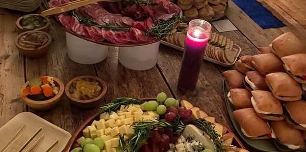 Charcuterie and sandwiches with a lit candle on a wooden table.