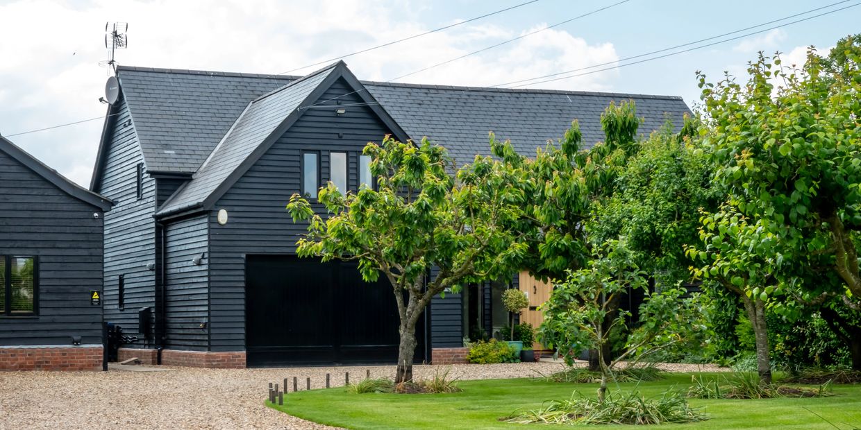 Modern black house with lush green trees and a gravel driveway.