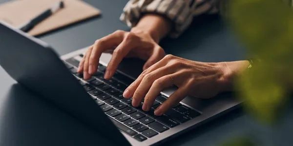 Hands typing on a laptop keyboard in a cozy setting.
