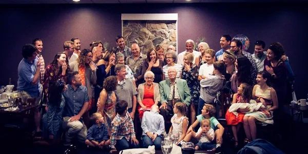 Large family gathered indoors for a joyful group photo around elderly couple.