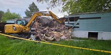 Excavator demolishing a blue mobile home.