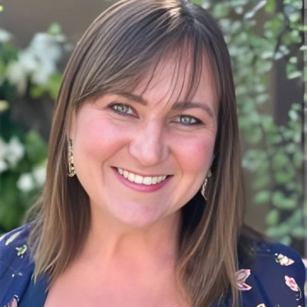 Smiling woman with shoulder-length hair and floral outfit in natural light.