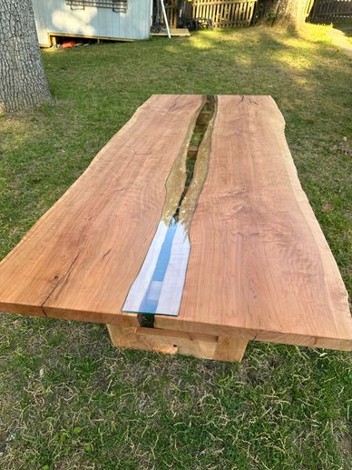 Wooden table with a clear resin river running through the center, set outdoors on grass.
