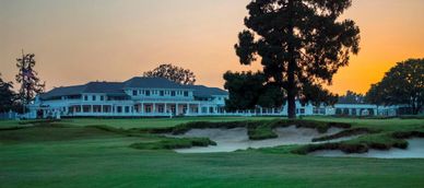 Golf course with clubhouse and sunset sky.