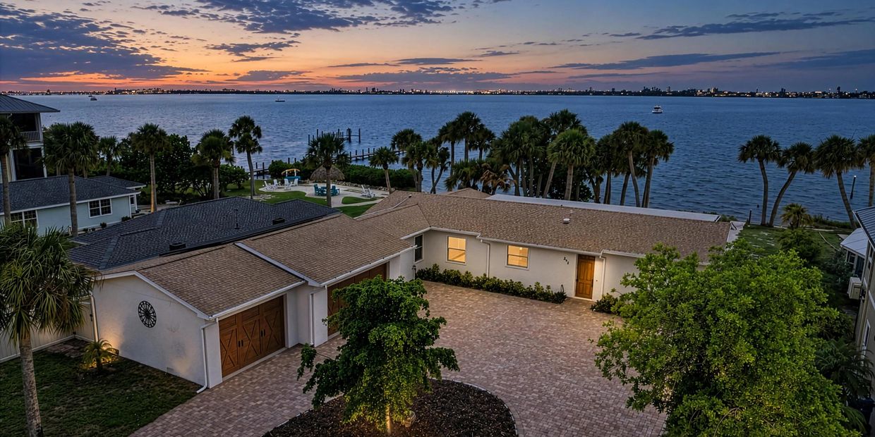 Waterfront house with sunset and palm trees.