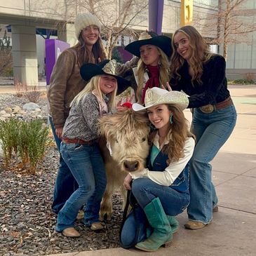 Rodeo queens gathered around a miniature cow during a community event, western culture