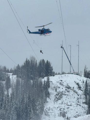 A helicopter airlifts a person above a snowy forested hillside.