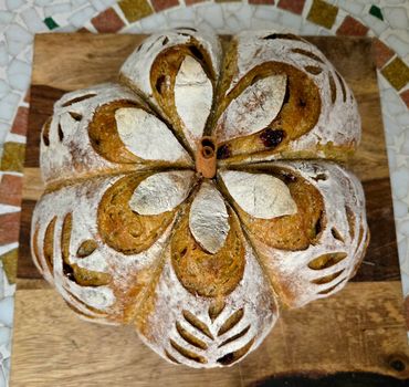 Artfully scored round loaf of bread with a cinnamon stick center on a wooden board.