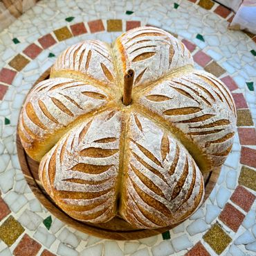 Artisan round bread with decorative leaf-like flour patterns and a cinnamon stick center.