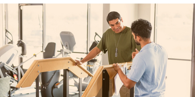 Two men discussing rehabilitation exercises using parallel bars in a gym.