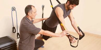 A trainer assists a man using suspension straps for exercise.