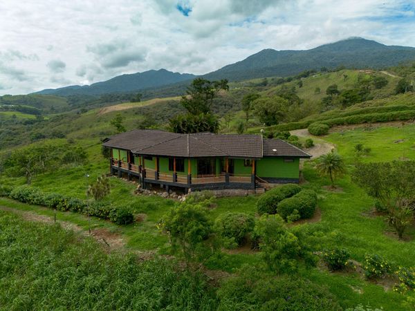 A green house surrounded by lush greenery and hills under a cloudy sky.