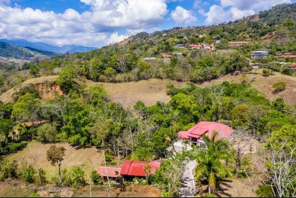 Hillside with houses and greenery under a cloudy blue sky.