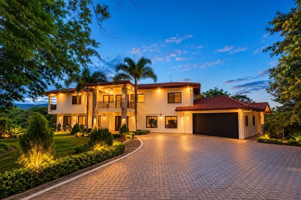 Luxurious two-story house with palm trees and warm exterior lighting at dusk.