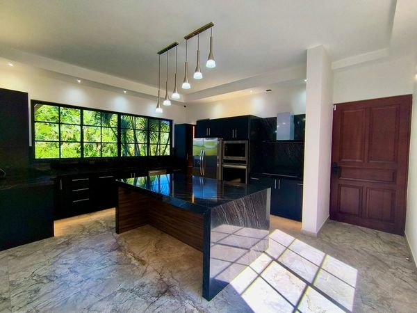 Modern kitchen with black cabinets and island, large window, and marble floor.