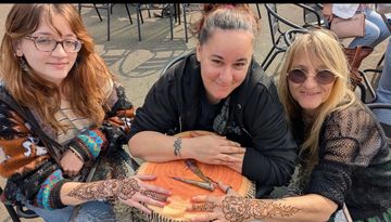 Professional henna artist creating custom henna designs for guests at an outdoor event.